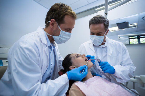 Dentists examining a female patient with tools at dental clinic